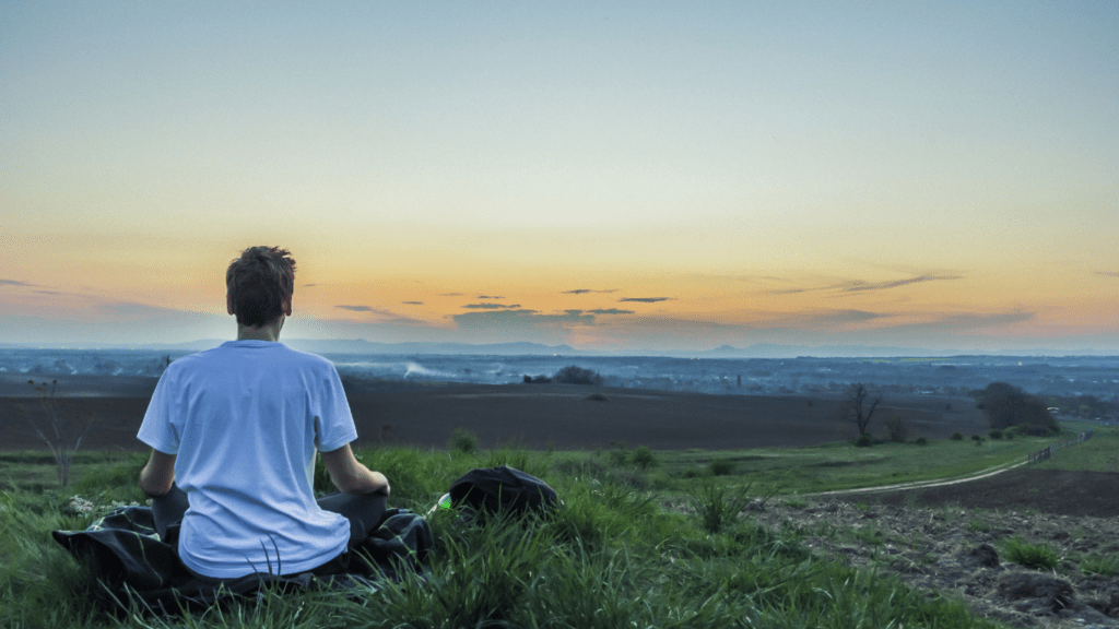 a person sitting on a hill overlooking the ocean at sunset