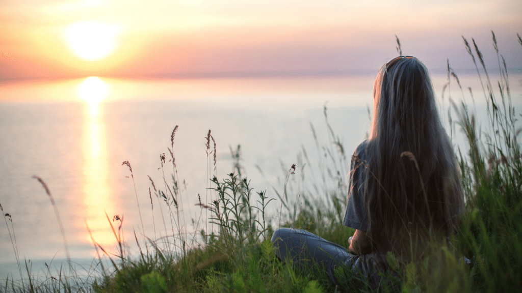 a person sitting on a hill overlooking the ocean at sunset