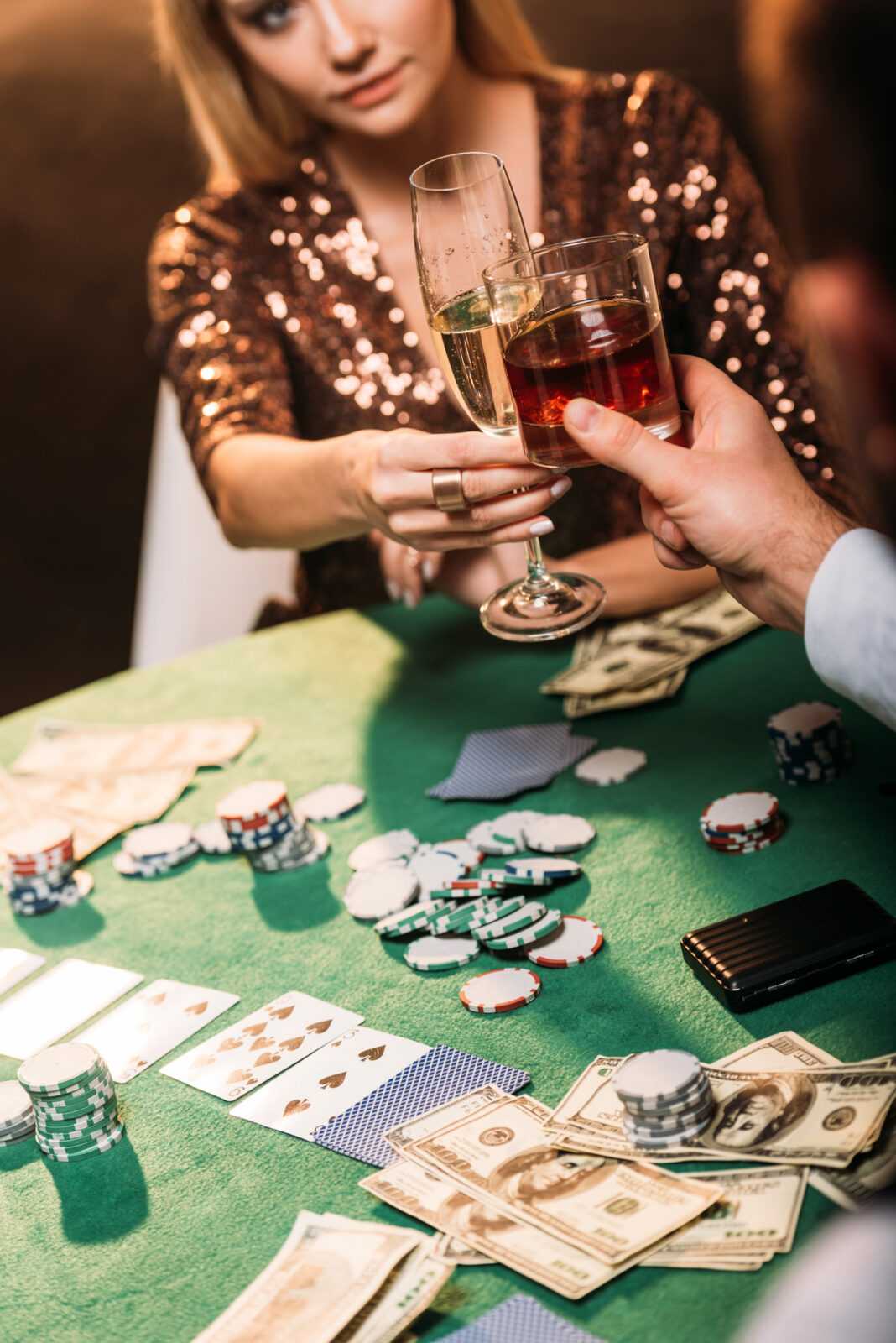 cropped image of girl and croupier clinking with glasses of alcohol drinks while playing poker at