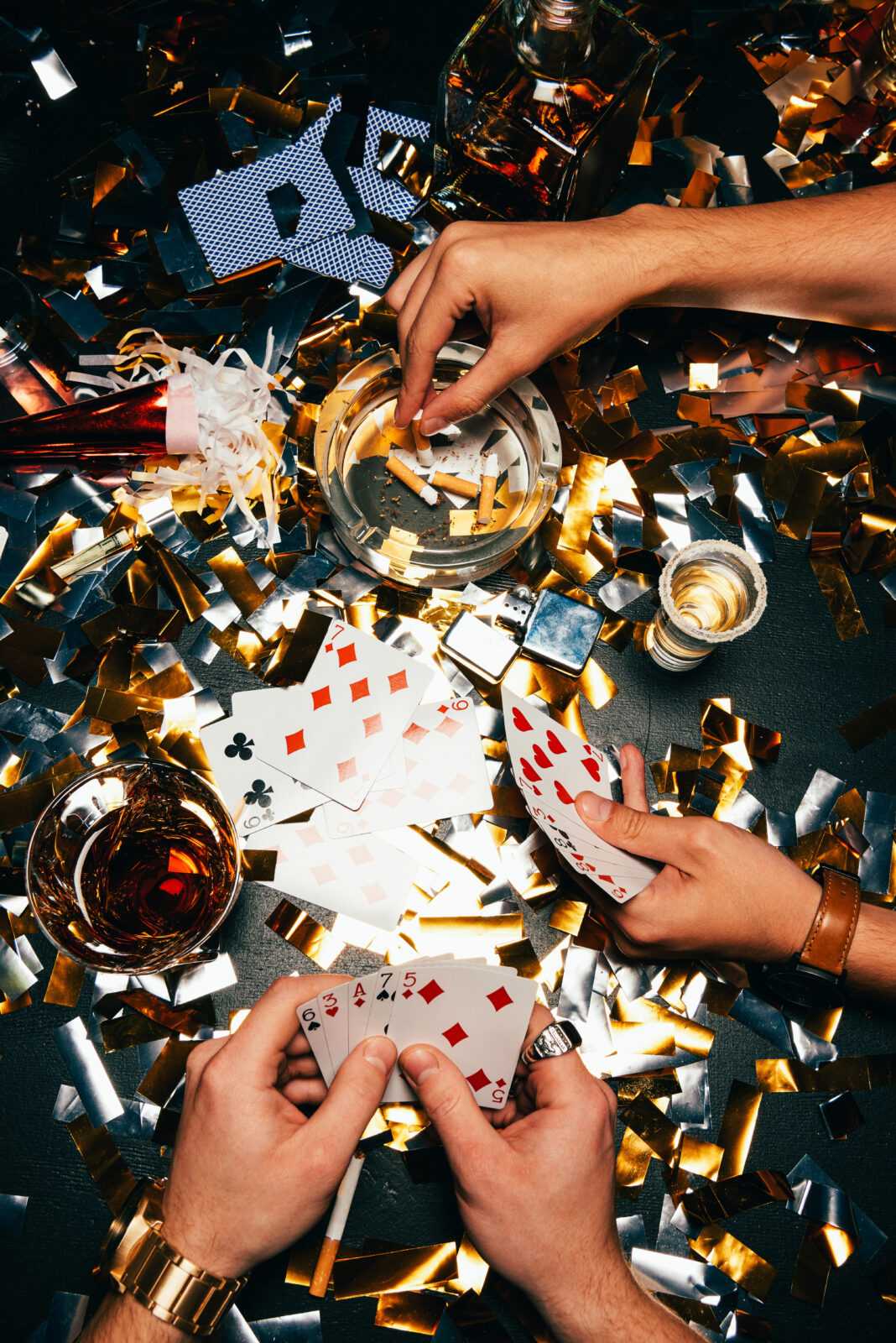 partial view of men smoking cigarettes and playing poker at table covered by golden confetti
